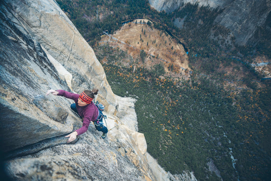 Pro climber Babsi Zangerl climbing a steep rock face with a mountainous landscape in the background